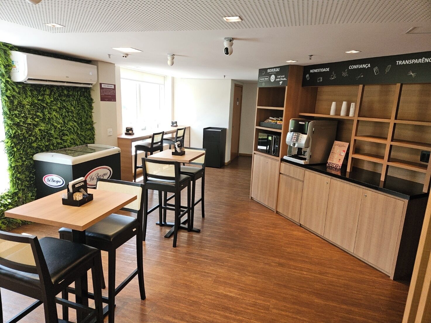 Un café con mesas y sillas de madera, una máquina de café y un aire acondicionado de pared.