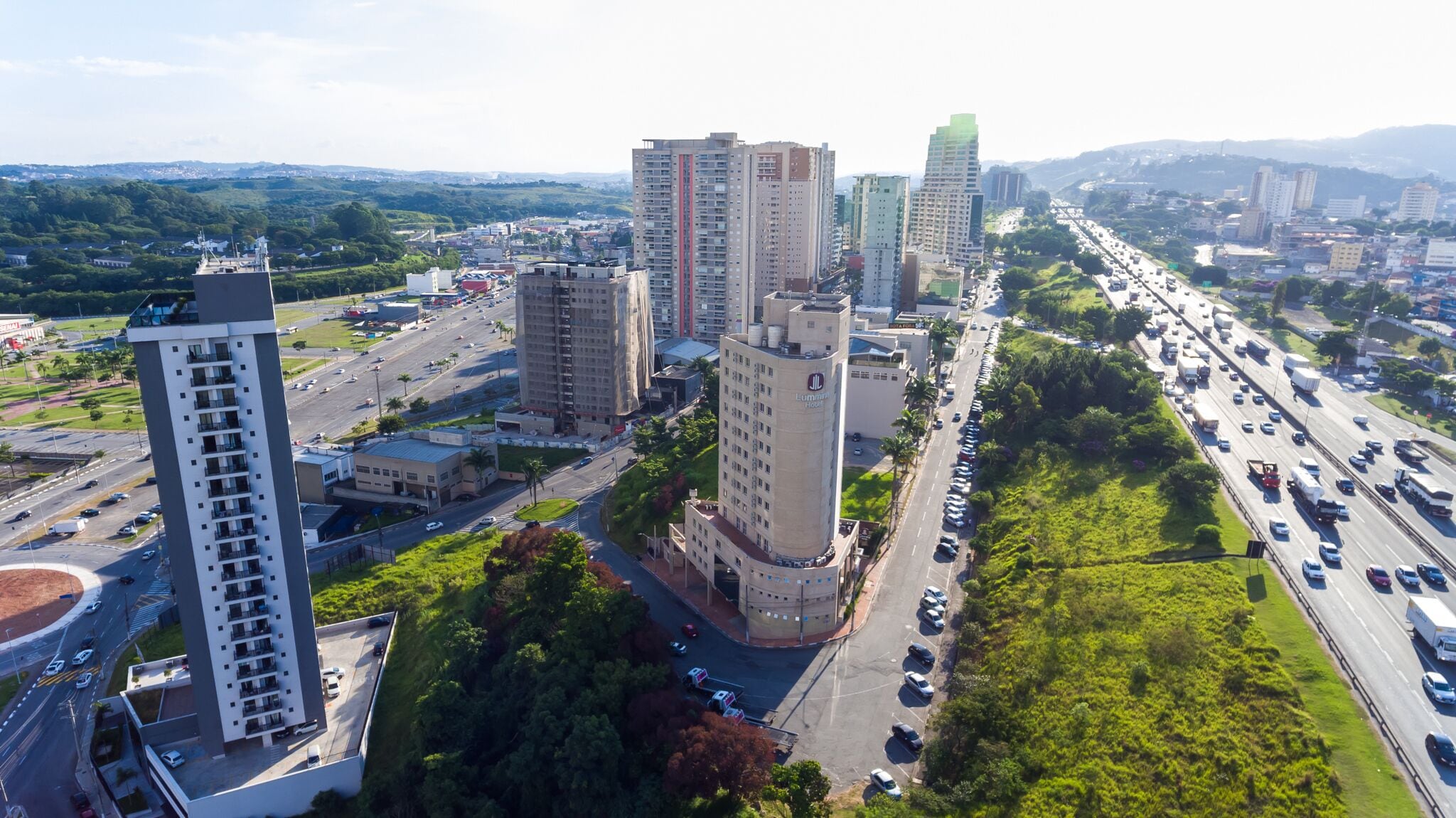 Un edificio de gran altura con varios pisos, rodeado de vegetación y una calle con mucho tráfico.