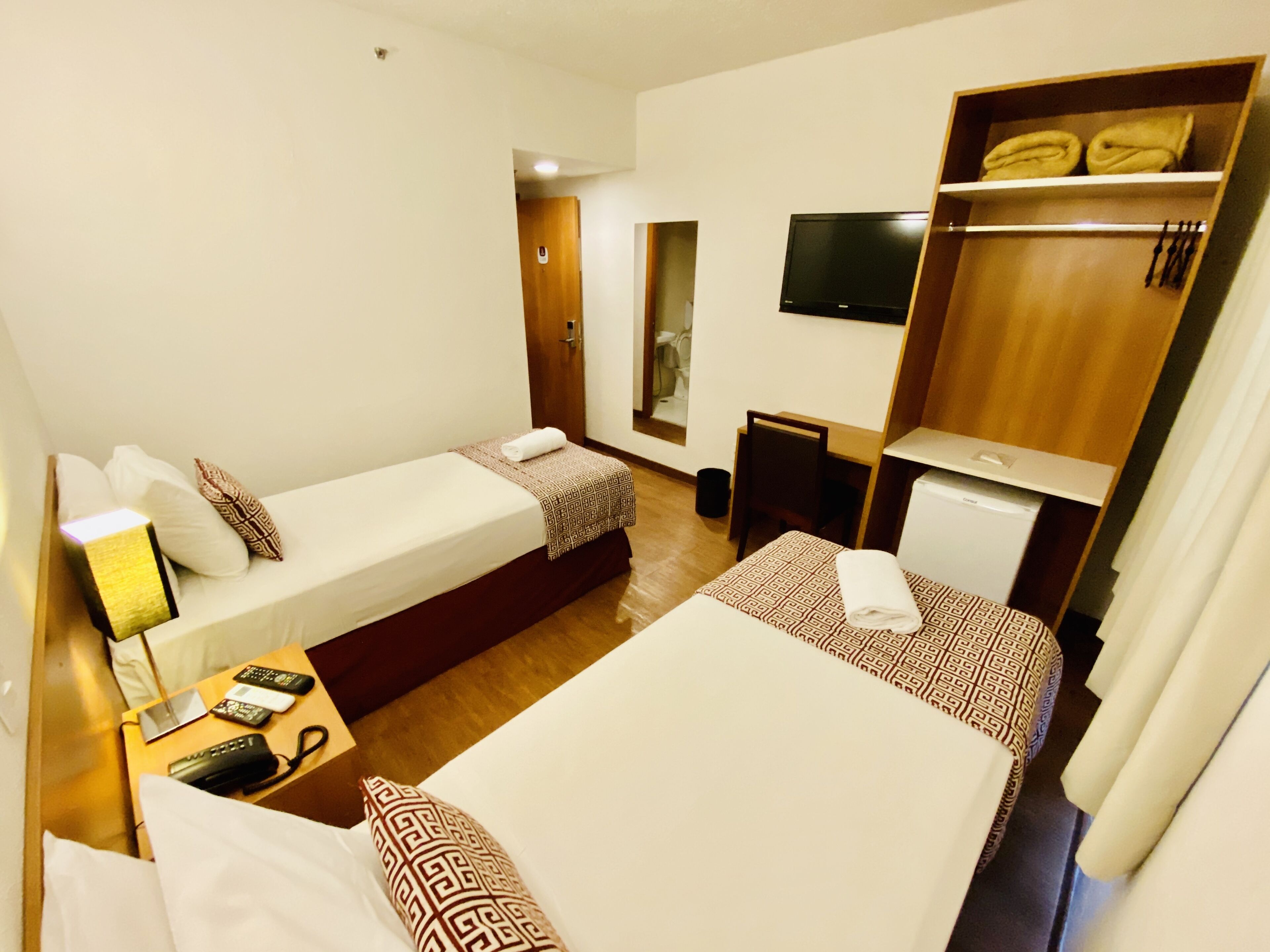 A hotel room with two beds, a desk with a chair, a television, and a wardrobe.