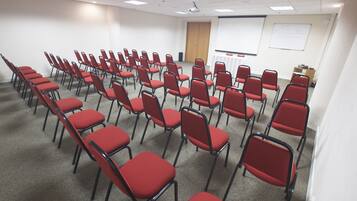 A conference room with rows of red chairs, a whiteboard, and a projector screen.