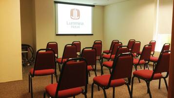 A conference room with red chairs arranged in rows, a projector screen displaying 'Lumma Hotel', and a ceiling with recessed lighting.