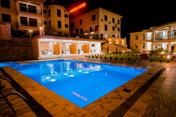 A hotel with a swimming pool, outdoor seating, and a well-lit facade.