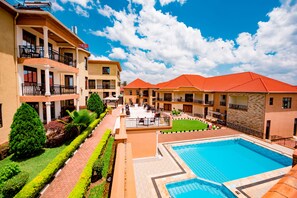 A hotel with multiple balconies, a swimming pool, and well-maintained gardens.