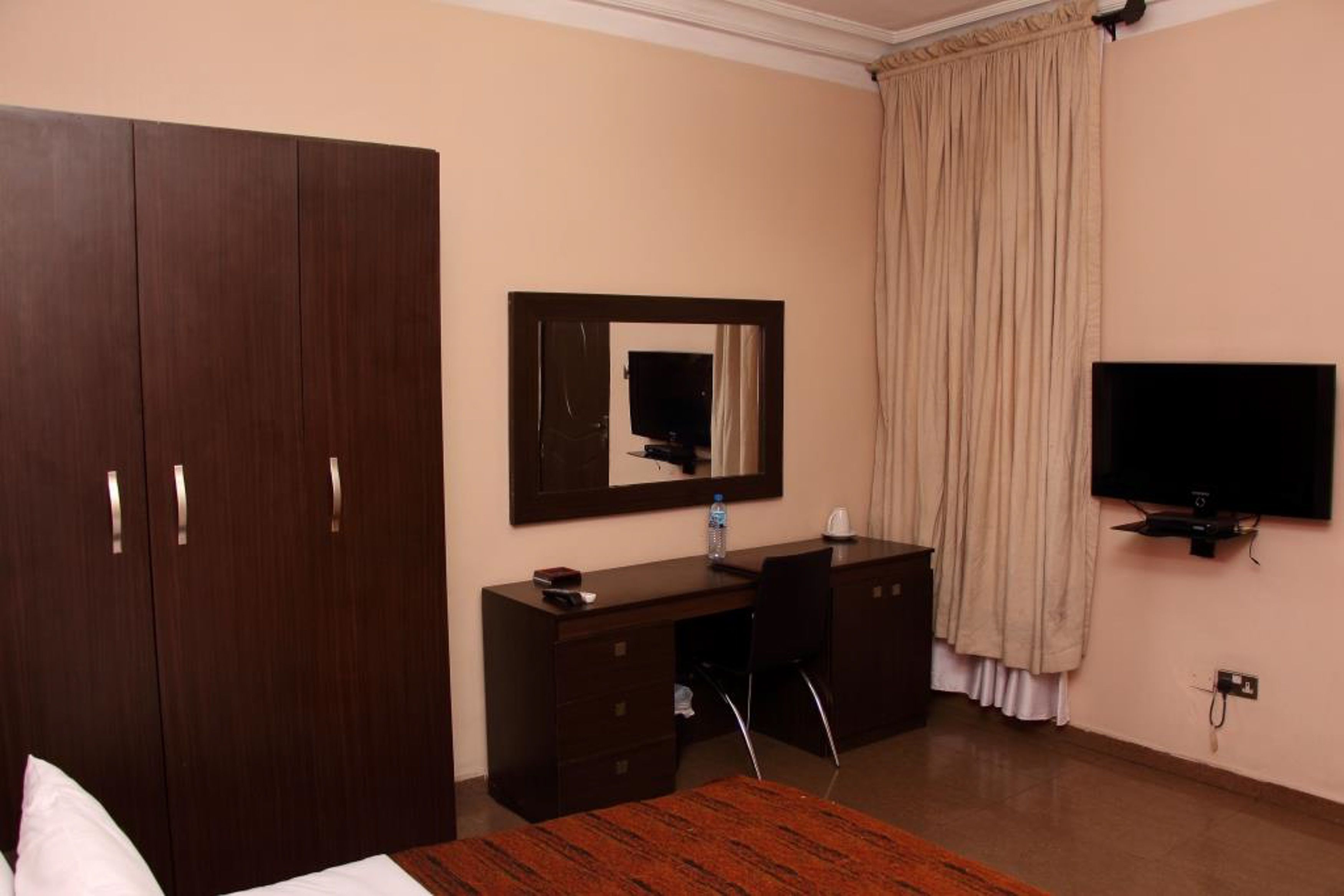 A hotel room with a large wardrobe, a desk with a chair, a television, and a bed.