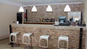 Baarialue, jossa on kiviseinä, kolme valkoista baarijakkaraa, tiski, jossa on kahvinkeitin, ja kyltti, jossa lukee: ”RESTAURANT INT”.