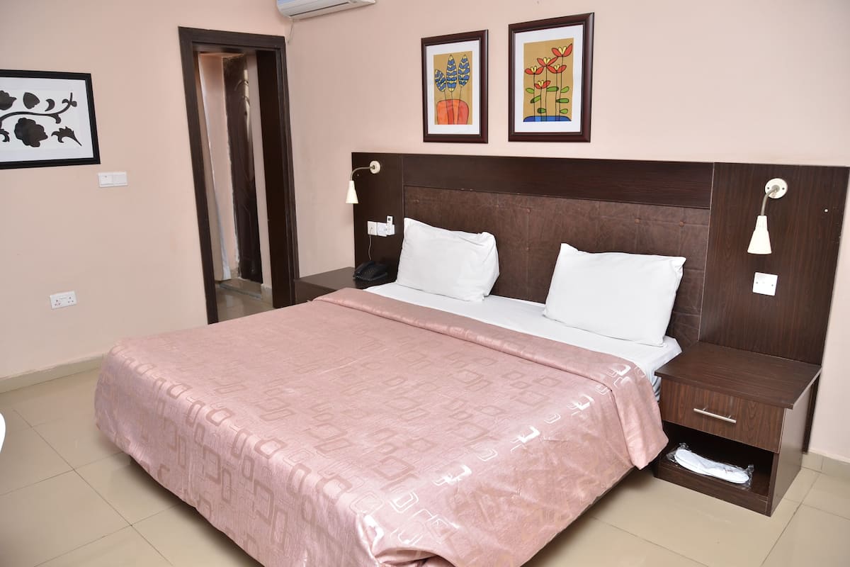 A neatly made bed with a pink patterned bedspread, a wooden headboard, and two bedside tables with lamps.