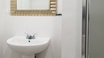 Un baño con un lavamanos blanco, un espejo con marco de madera y una zona de ducha.