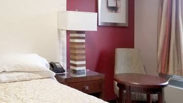 A hotel room with a bed, a bedside table with a lamp, a chair, and a framed picture on the wall.