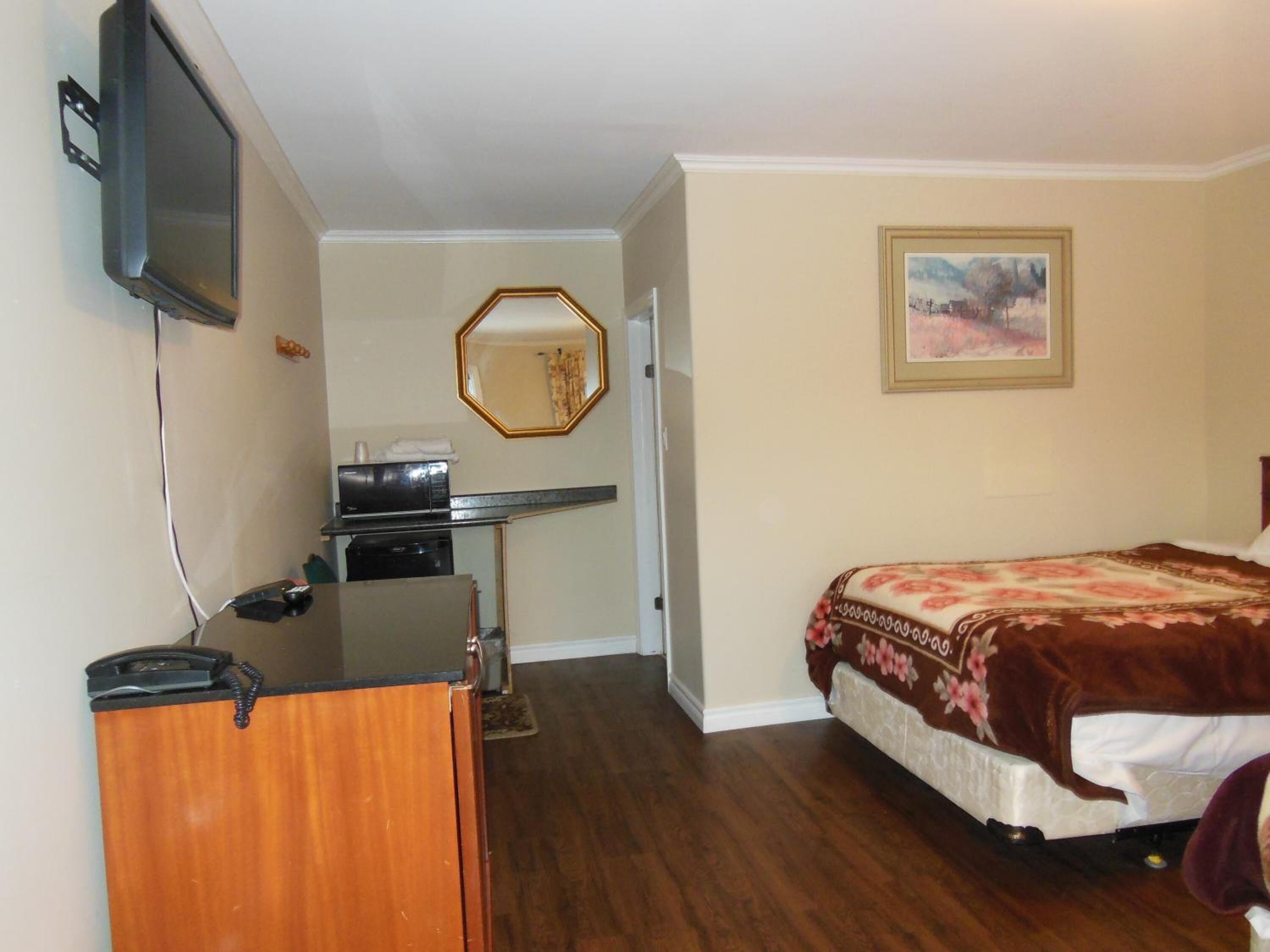 Une chambre d’hôtel avec un lit, un bureau avec un ordinateur, un miroir et un tableau au mur.