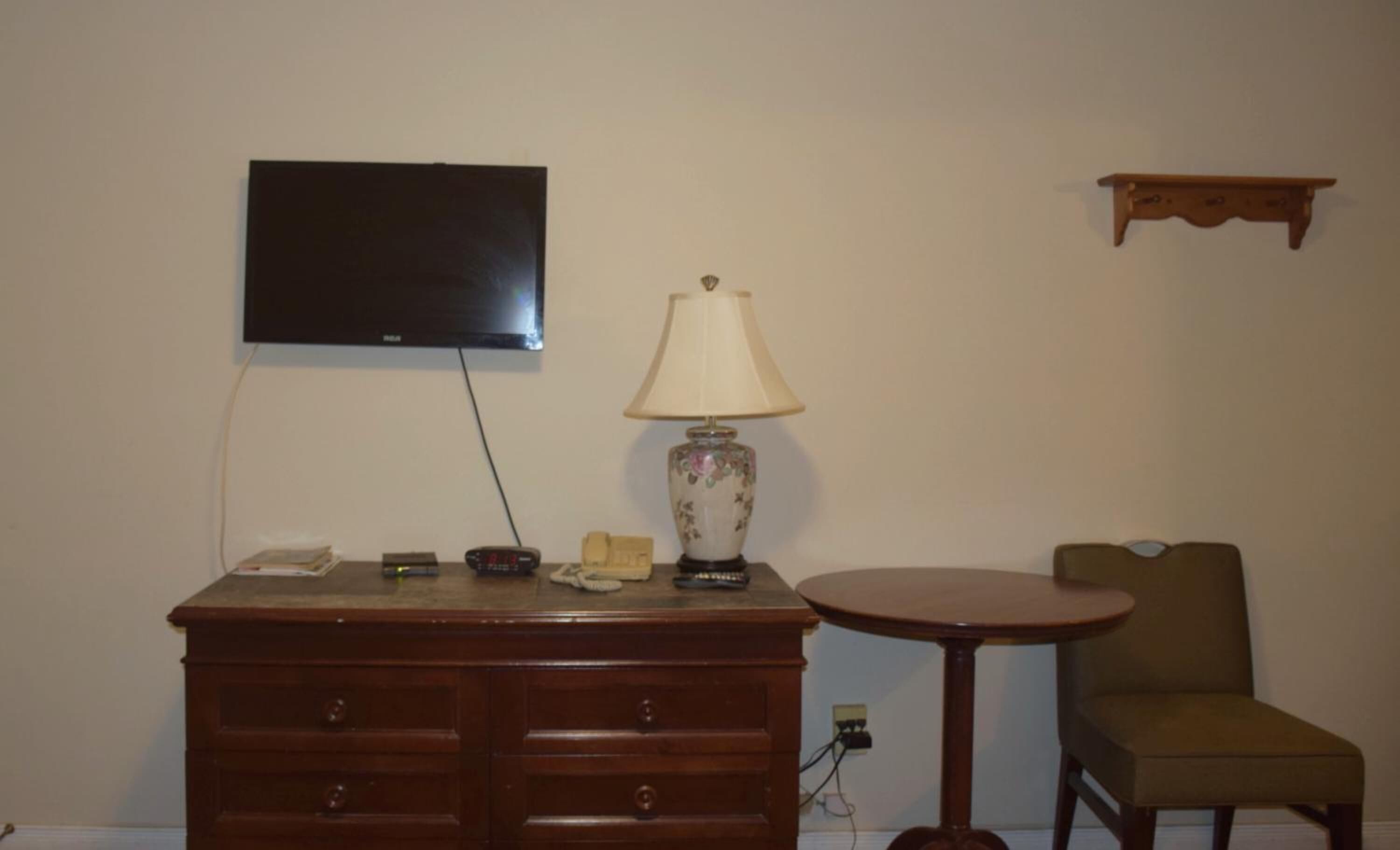 Una habitación con un aparador de madera, una mesa con lámpara, un televisor en la pared y una silla.