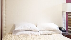 A bed with a white quilted cover and two white pillows.