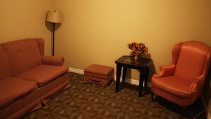 A living room with a sofa, ottoman, armchair, and a small table with a vase of flowers.