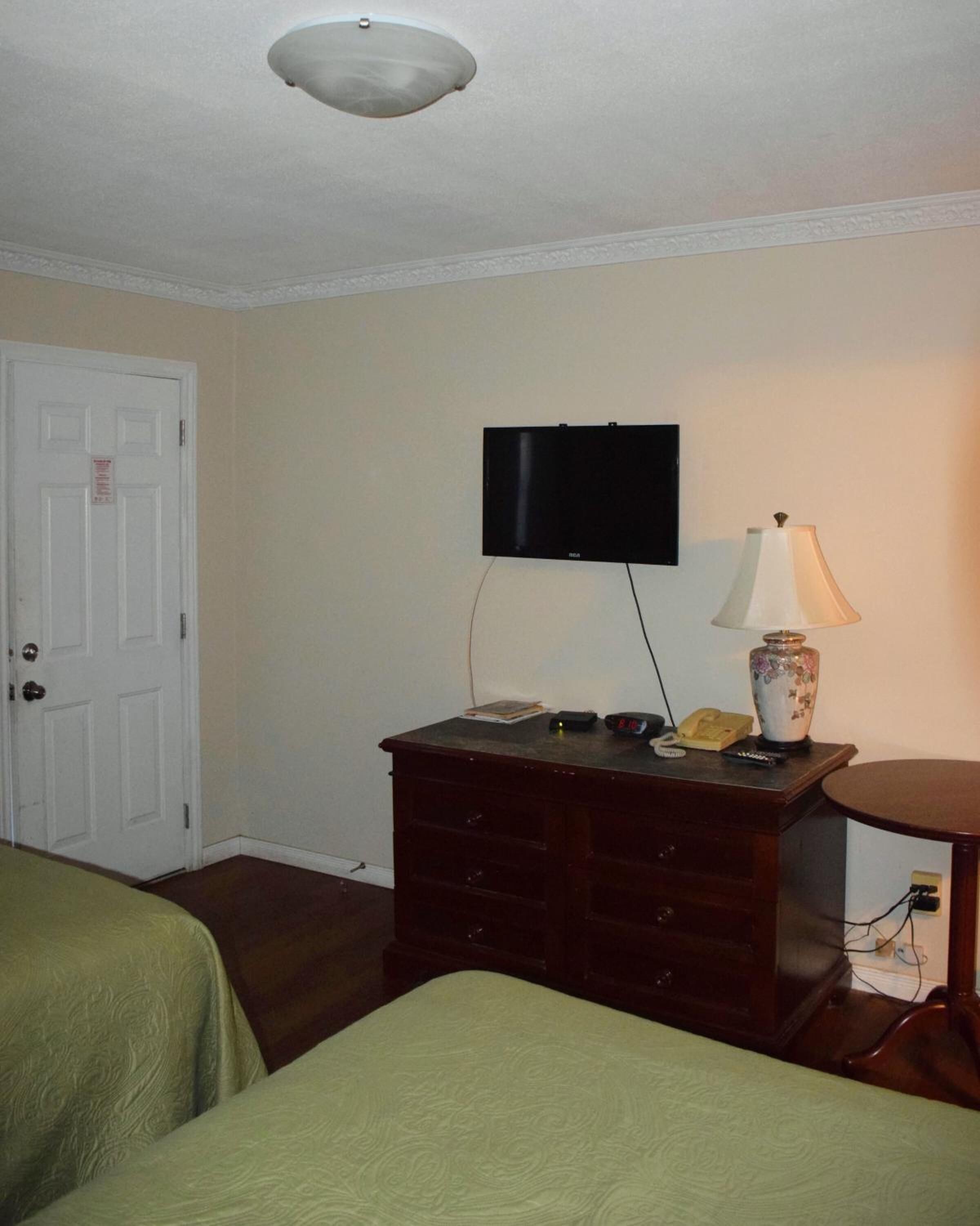 A room with two beds, a TV mounted on the wall, a wooden dresser, and a lamp.