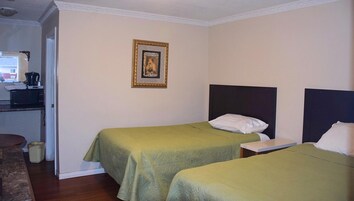 Habitación de hotel con dos camas individuales, un escritorio pequeño con silla, microondas y cafetera.