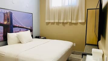 Habitación de hotel con cama, televisor mostrando una vista urbana, ventana con cortinas translúcidas y una pequeña mesa con bandeja.
