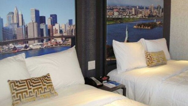 Habitación de hotel con dos camas, ropa de cama blanca y vista a la ciudad.