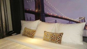 Una cama con dos almohadones estampados, un edredón blanco y vista a un puente de noche.