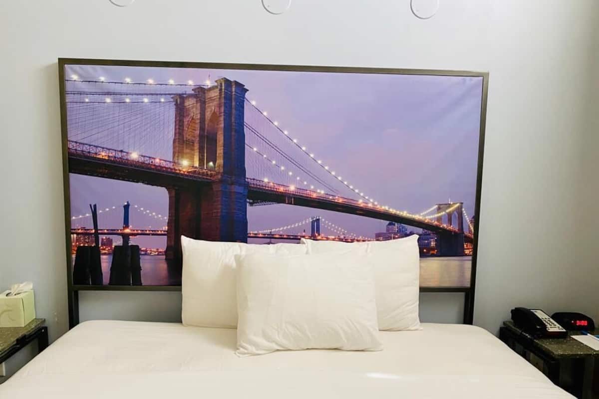 A hotel room with a large bed, white pillows, and a view of a bridge at night.