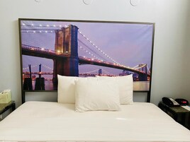 Habitación de hotel con una cama grande, almohadas blancas y vista a un puente de noche.