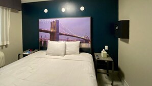 Habitación de hotel con una cama grande, una mesita de noche, un televisor y una lámpara fijada a la pared.
