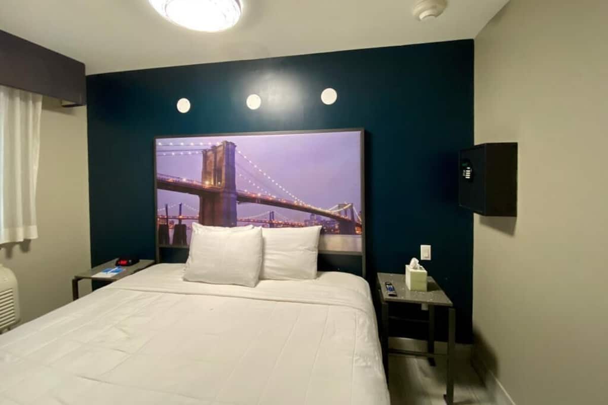 A hotel room with a large bed, a nightstand, a TV, and a wall-mounted light fixture.