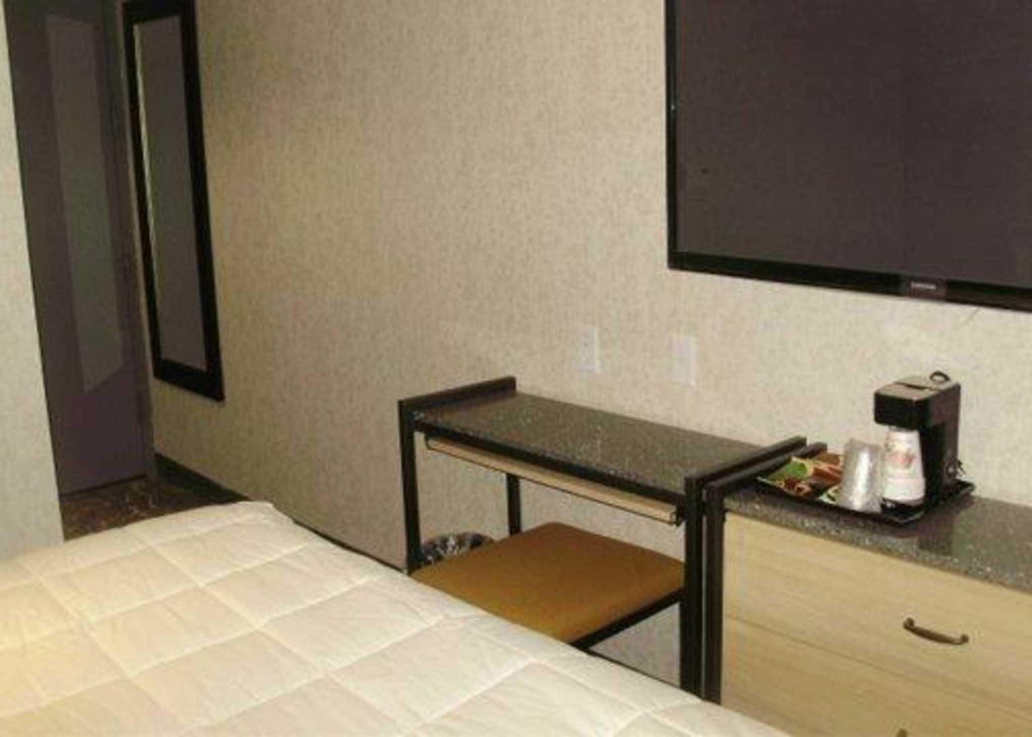 Ein Hotelzimmer mit einem Bett, einem kleinen Schreibtisch mit Stuhl, einer Kaffeemaschine und einem an der Wand montierten Fernseher.