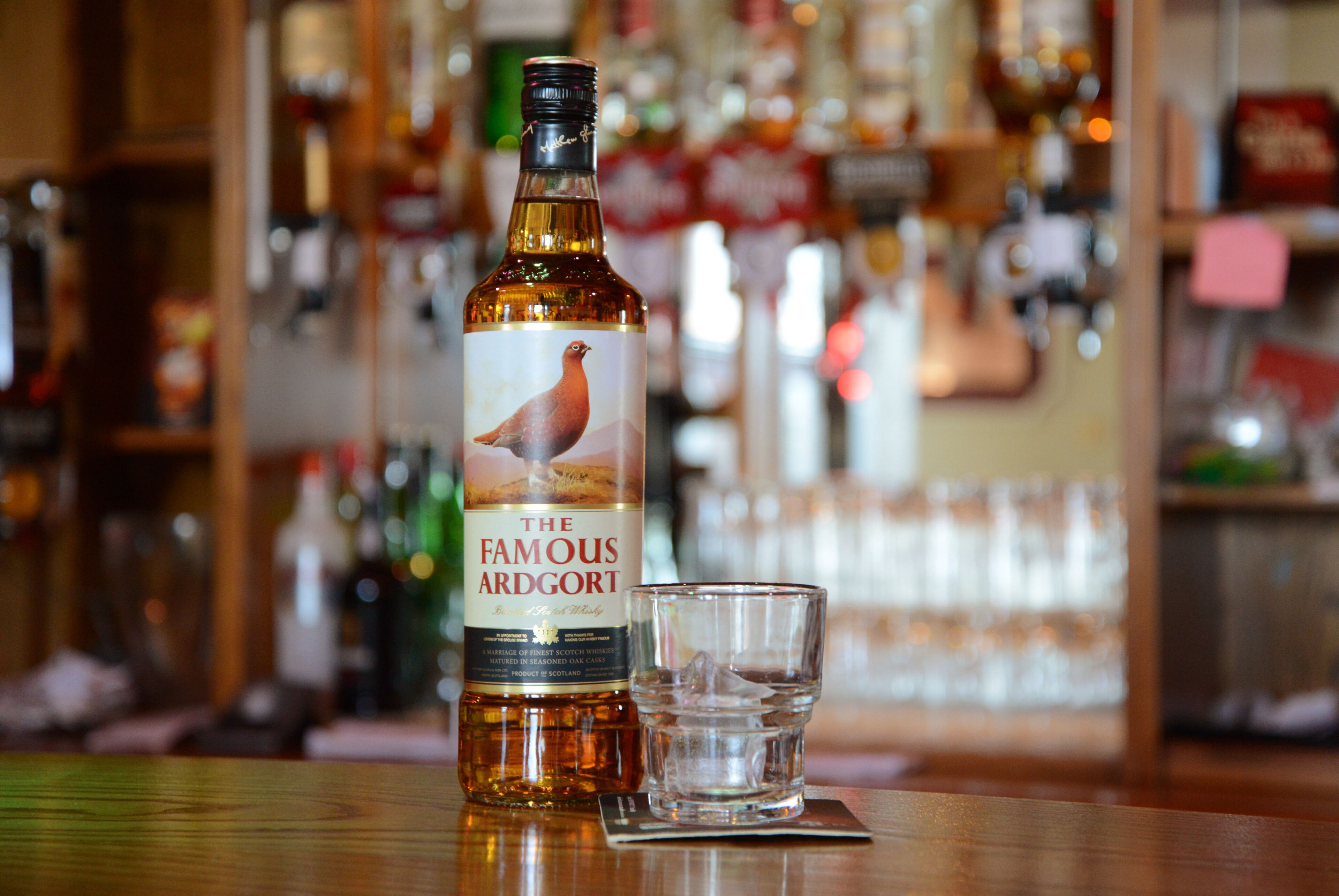 Een fles Famous Ardort whisky en een glas op een bar.