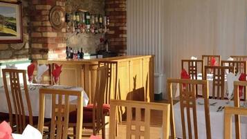 A dining area with wooden chairs and tables, a brick wall with a wine rack, and a window with blinds.