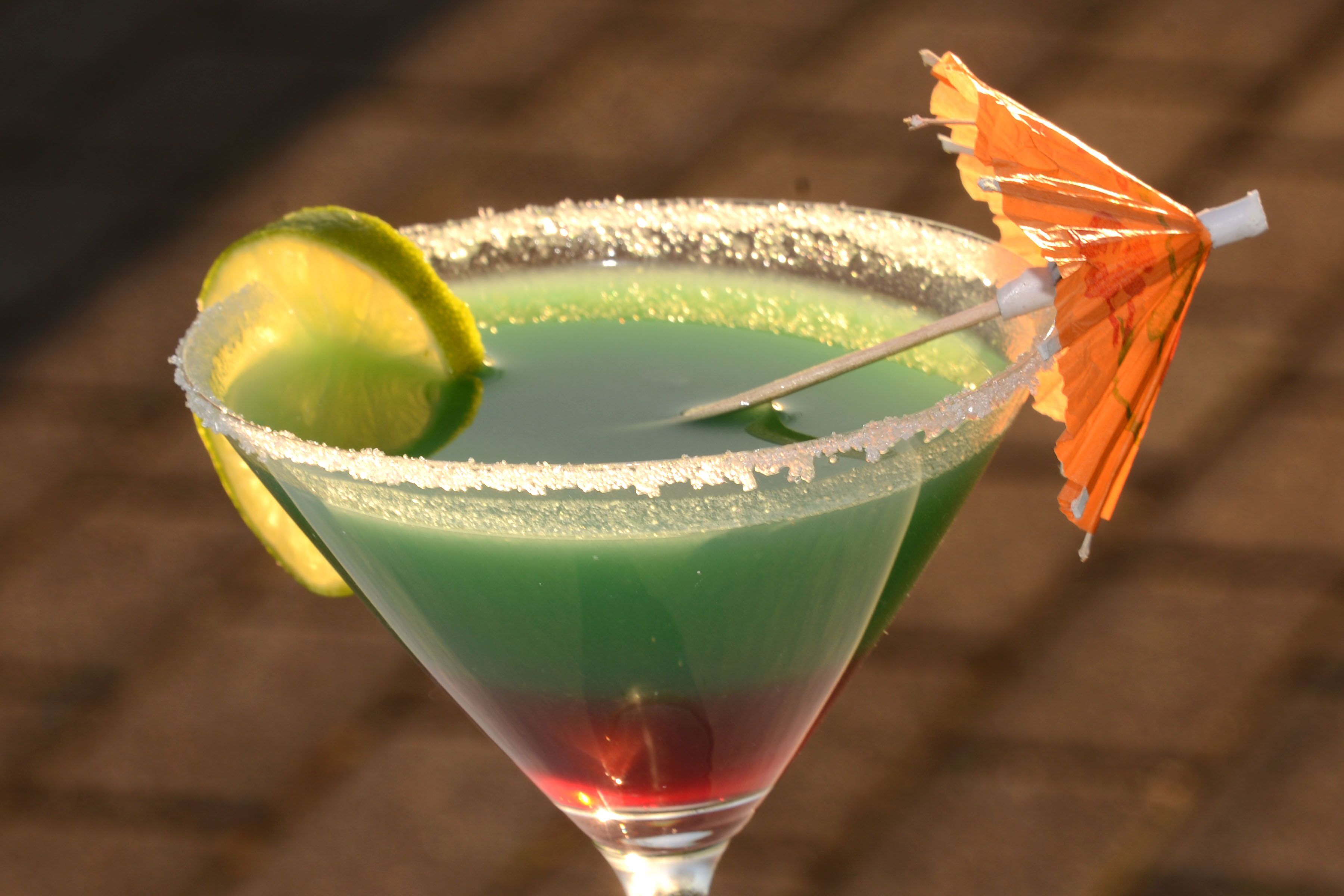 A cocktail in a martini glass with a salted rim, lime wedge, and an orange umbrella.