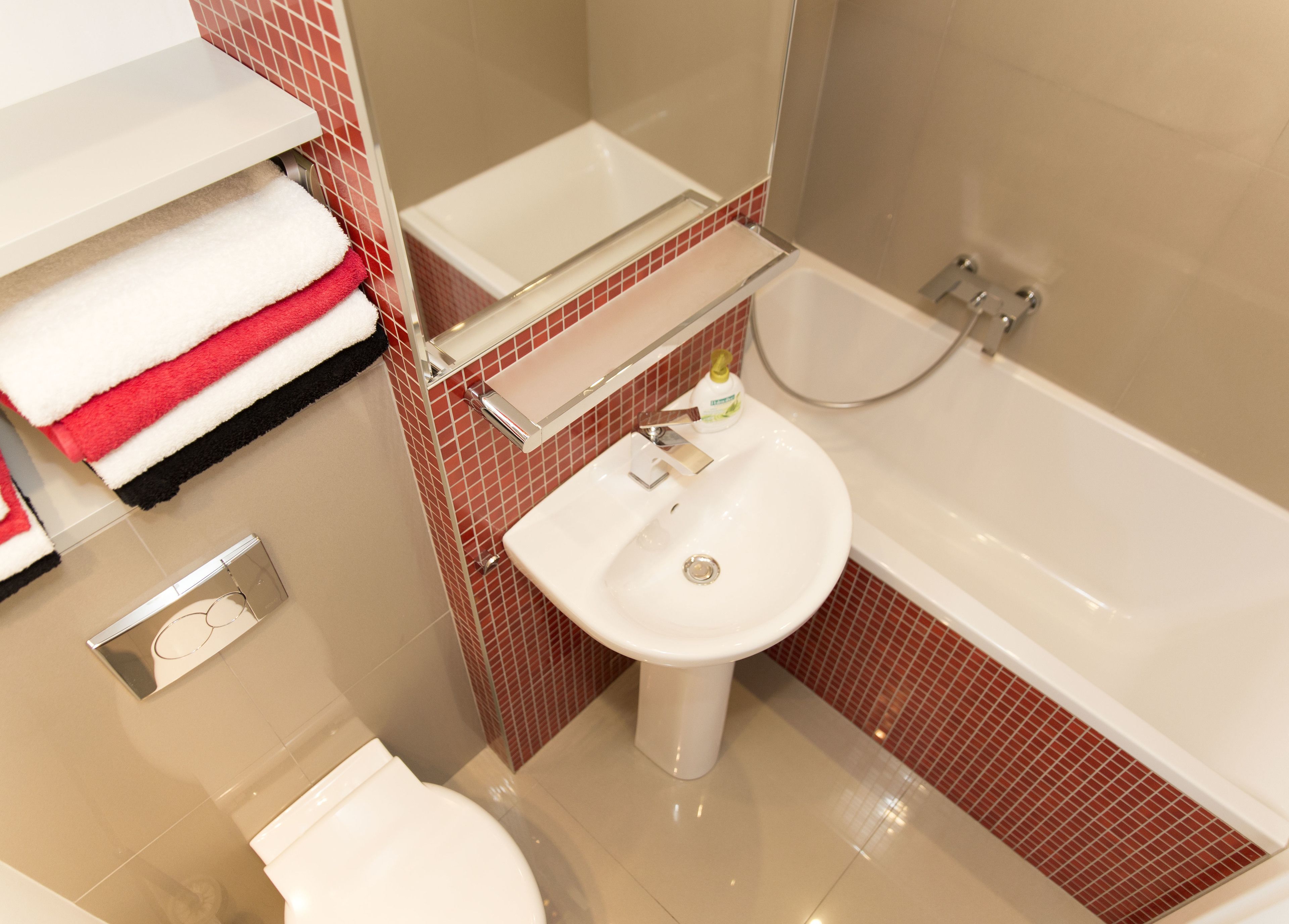 Un baño con un lavamanos blanco, una bañera y un inodoro. Hay toallas en un estante y un dispensador de jabón en el lavamanos.
