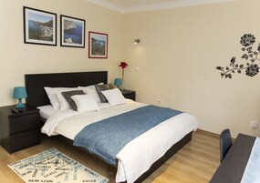 Une chambre bien rangée, avec un lit, des tables de chevet, un bureau et une chaise. On peut y voir des tableaux encadrés accrochés au mur, un vase avec une fleur et un motif décoratif sur le mur.