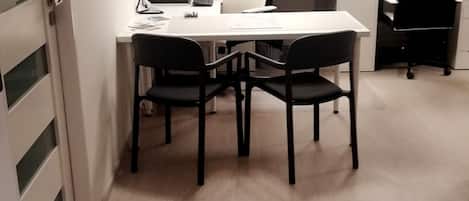 A modern office space with a white desk, black chairs, and a computer. There is a door on the left and a window in the background.