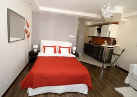 A modern hotel room with a large bed, a separate kitchenette, and a small dining area.