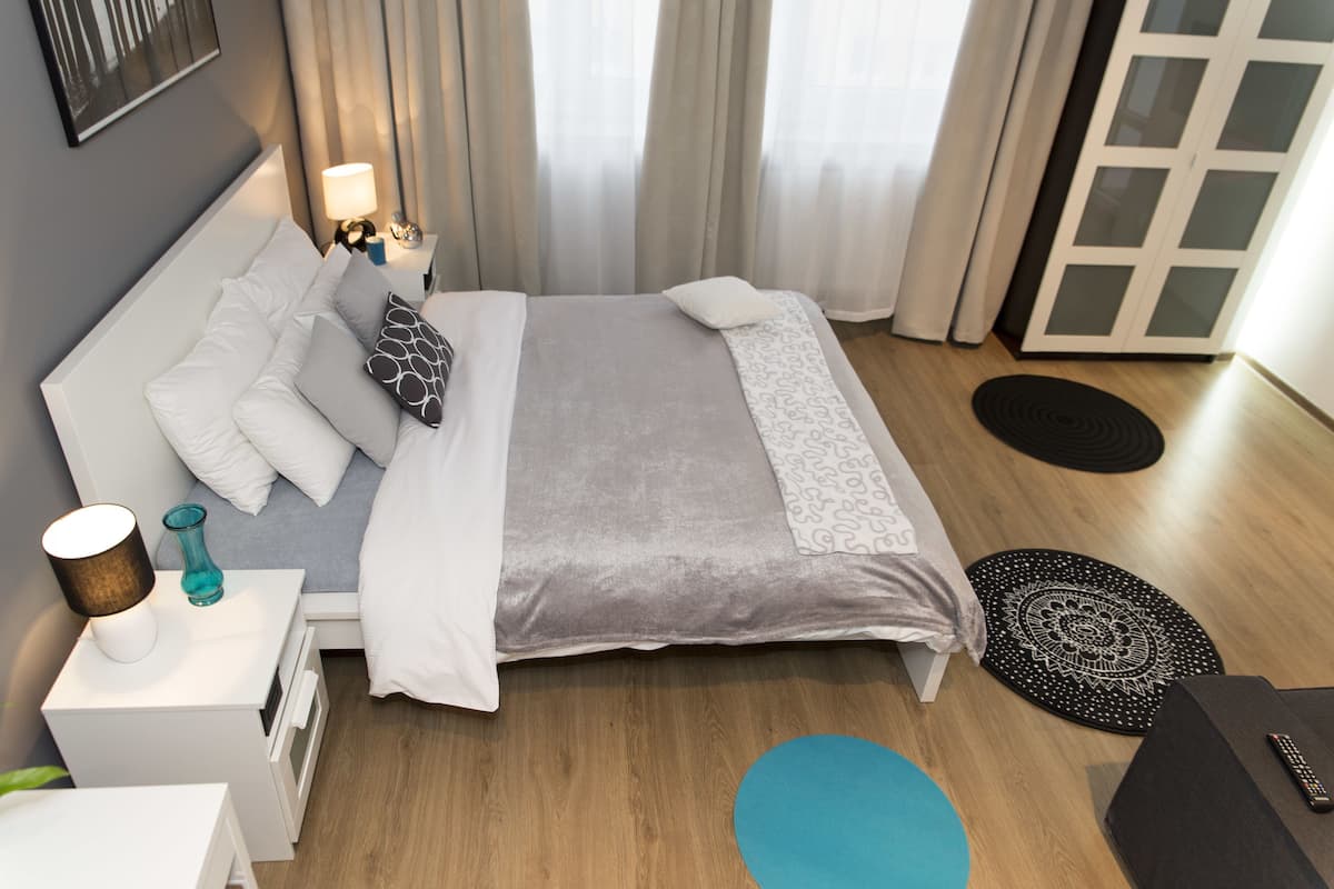 Une chambre d’hôtel moderne avec un lit soigneusement fait, une table de chevet avec une lampe, une petite table d’appoint avec un vase, et une vue sur l’extérieur par une porte.