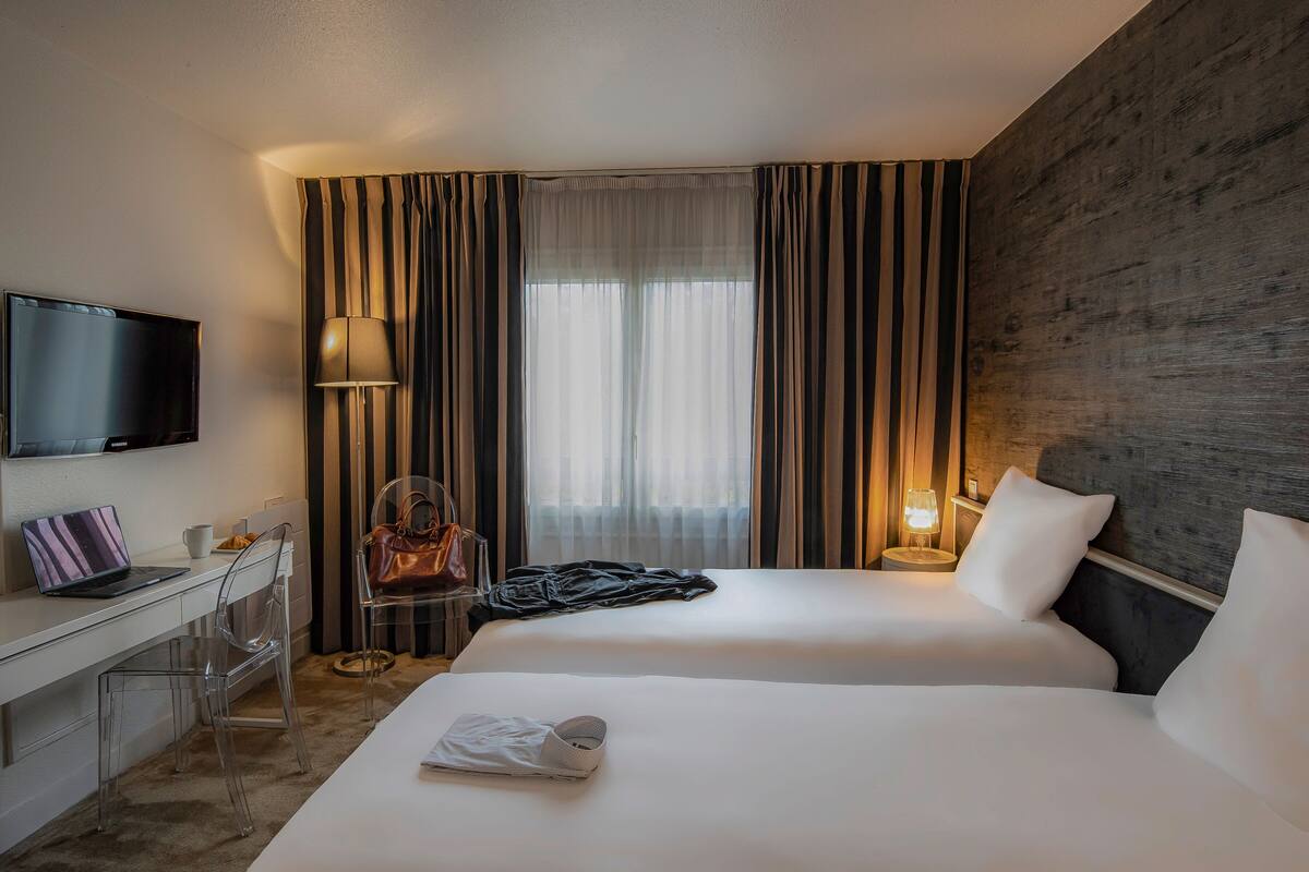 A hotel room with two beds, a desk with a laptop, a TV, and a chair.