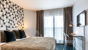 Habitación de hotel con una cama grande, un escritorio con una silla, un televisor y una pared con estampado geométrico.