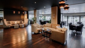 Un hallo amplio con piso de madera, un conjunto de sofás y una zona de comedor con mesas y sillas.