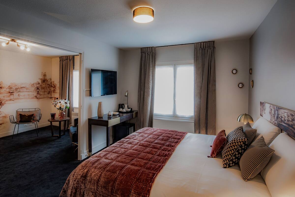 A hotel room with a large bed, a desk with a chair, a TV, and a window with curtains.
