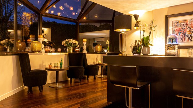 Zona de bar moderna con techo de cristal, suelo de madera y taburetes negros.