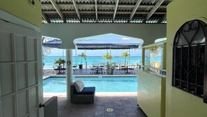 A covered outdoor area with a pool, lounge chairs, and umbrellas overlooking the ocean. - Osprey Beach Hotel (Cockburn Town)