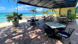 An outdoor patio with tables and chairs, a beach view, and potted plants. - Osprey Beach Hotel (Cockburn Town)