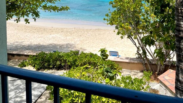 A beach view with clear turquoise water, palm trees, and a sandy shore. - Osprey Beach Hotel (Cockburn Town)