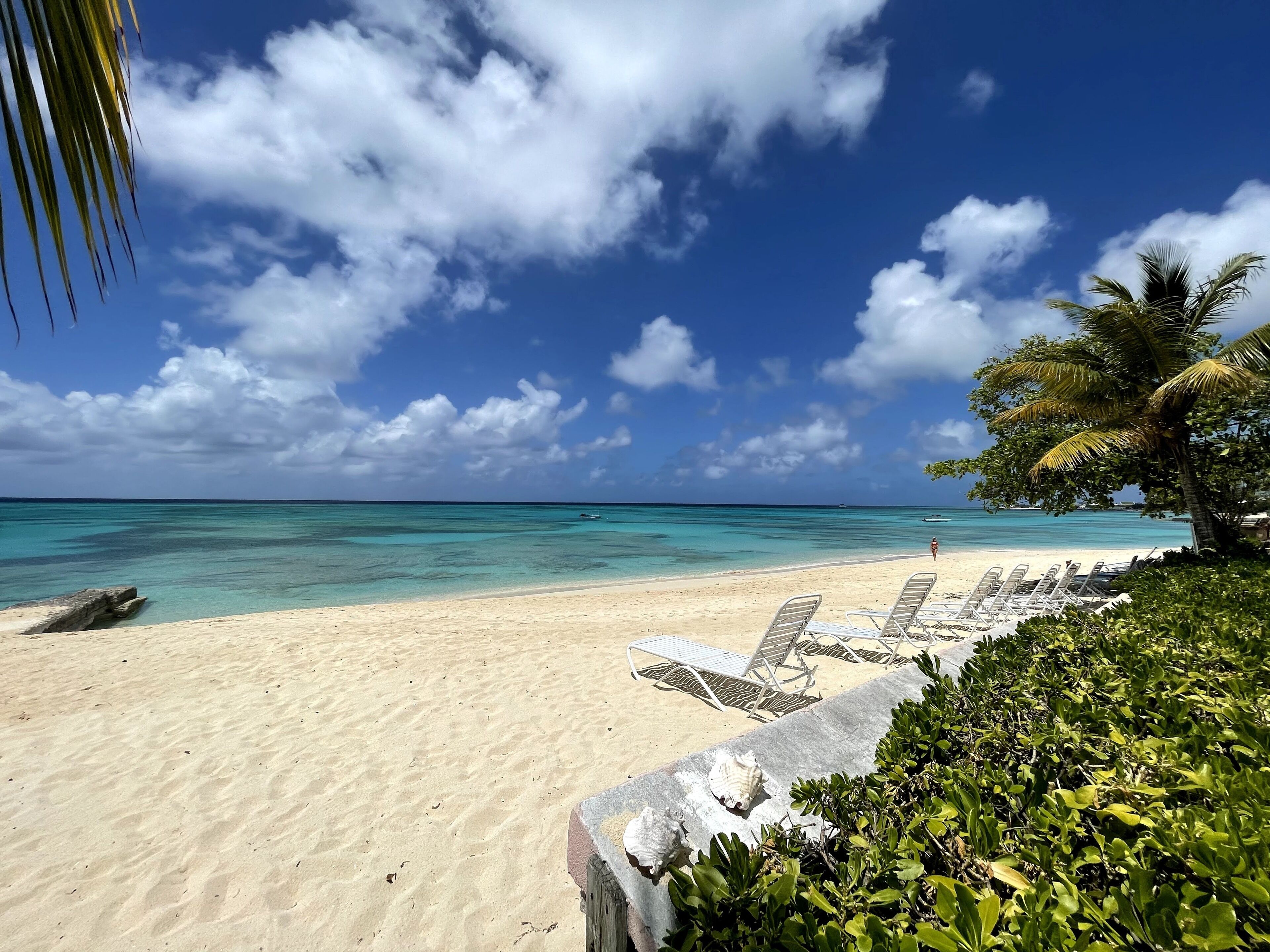 A beach with clear turquoise water, a sandy shore, and lounge chairs.