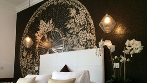 A bedroom with a large bed, two bedside lamps, a decorative wall mural, and a potted orchid plant. - Hotel Villa Rose (Nice)