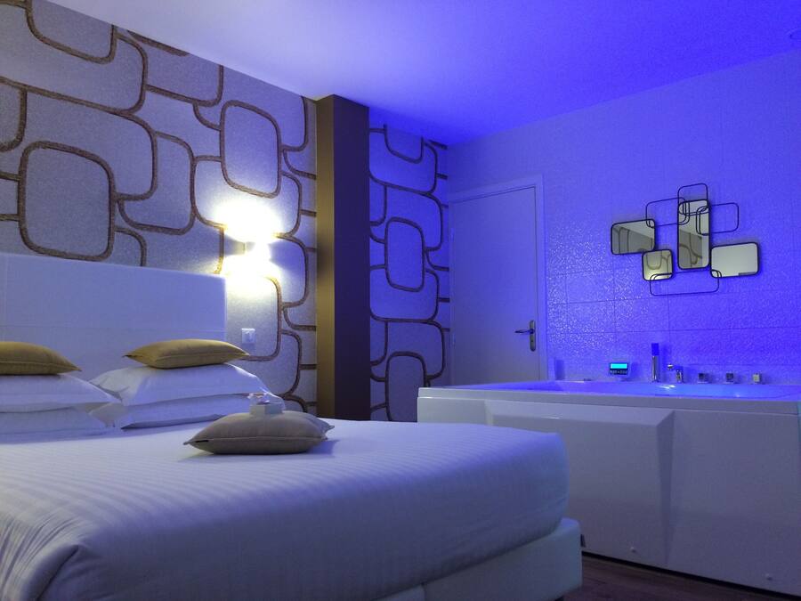 Une chambre d’hôtel moderne dotée d’un grand lit, d’une baignoire intégrée et d’un mur orné d’appliques murales aux formes géométriques.