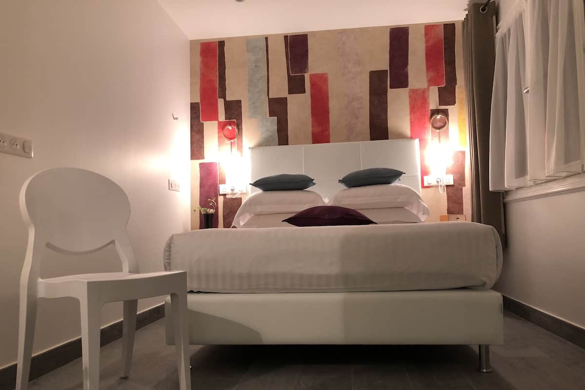 A modern hotel room with a large bed, a white chair, and a decorative wall.