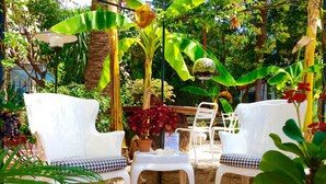 A wooden deck with white chairs and a table, surrounded by lush greenery and a hanging glass orb. - Hotel Villa Rose (Nice)