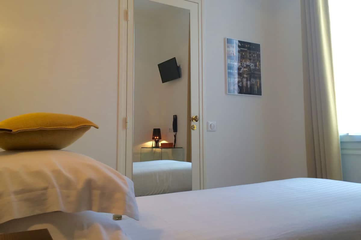 A hotel room with a bed, a bedside table with a lamp, a door, and a wall-mounted picture.