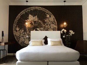 A bedroom with a large bed, two bedside lamps, a wall tapestry, and a vase with flowers. - Hotel Villa Rose (Nice)