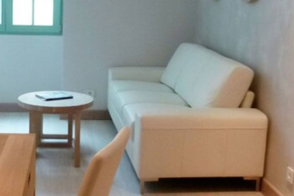 Una habitación pequeña y acogedora con una mesa de madera, una mesita redonda y un sofá de color claro.